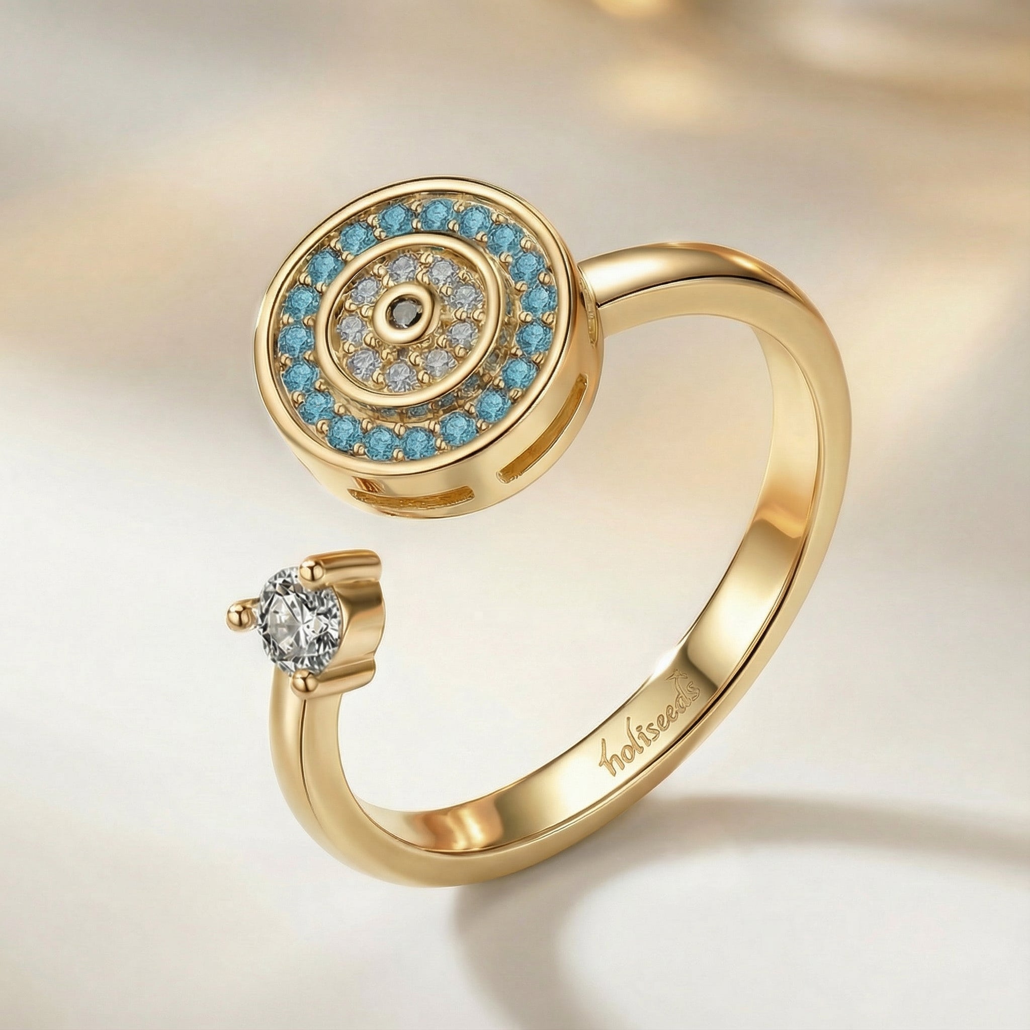 Bague dorée rotative Onde Azur Holiseeds au motif circulaire, ornée de pierres bleues et de détails lumineux.